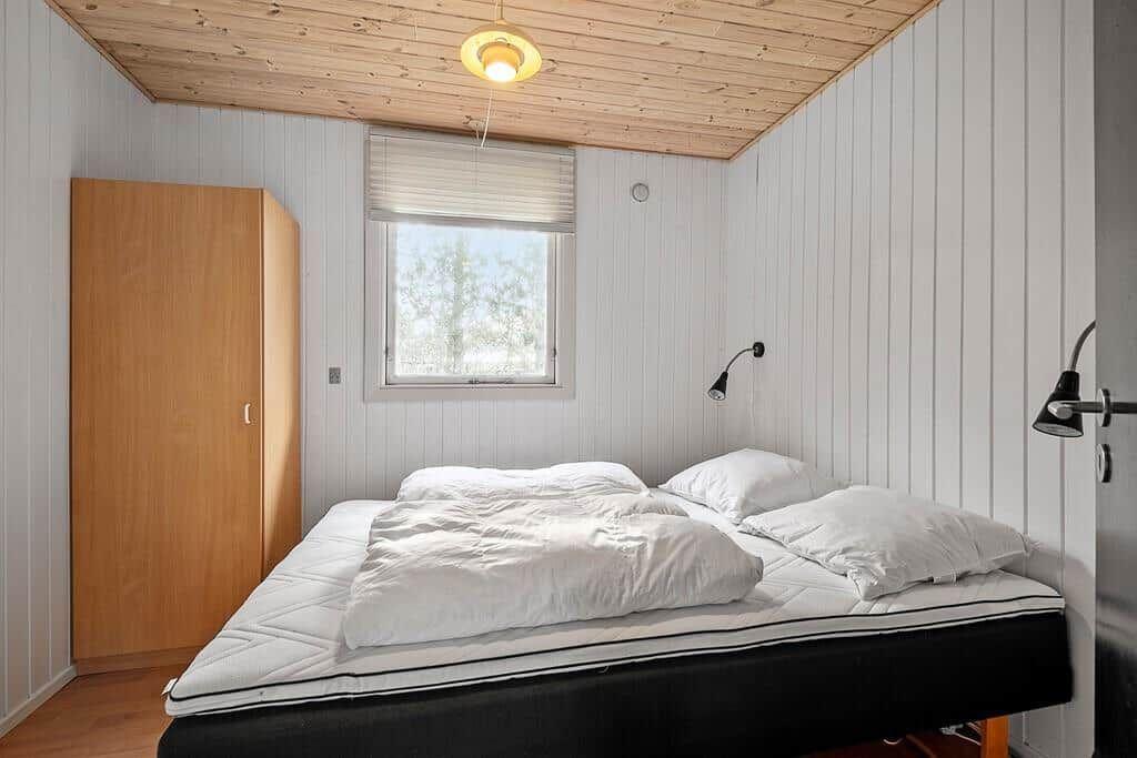 Schlafzimmer mit Bett, Kleiderschrank und Fenster. Holzdecke und weiße Wände.