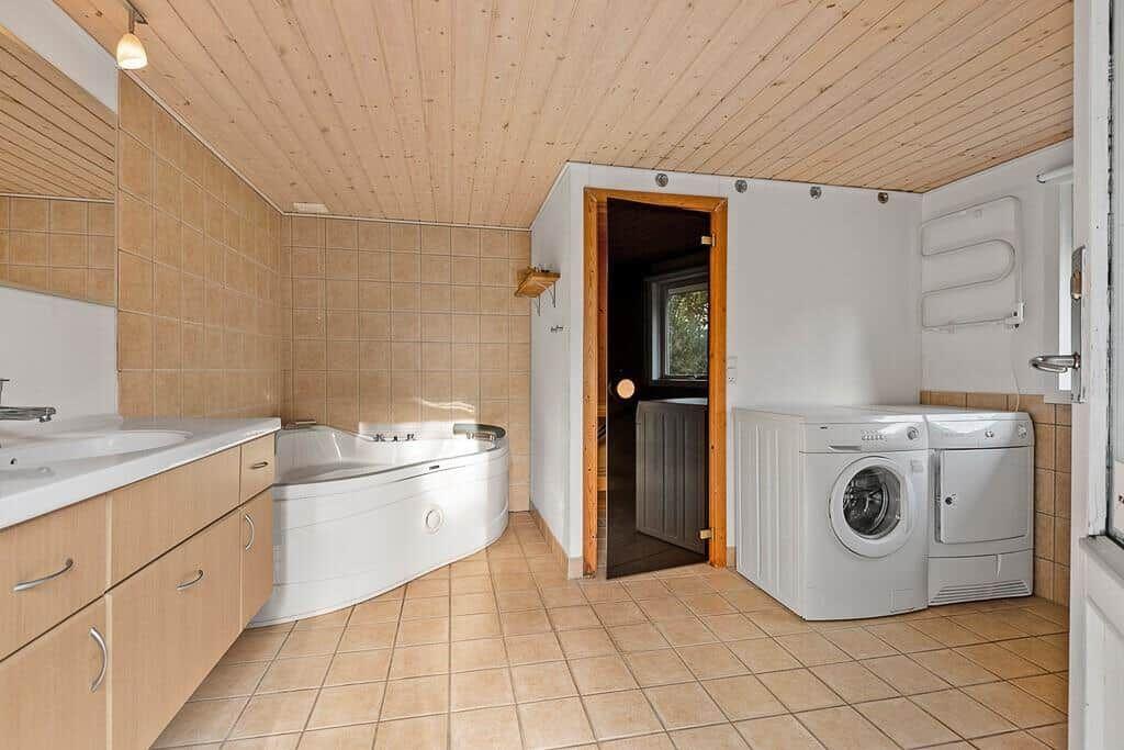 Badezimmer mit Whirlpool, Waschmaschine und Trockner. Holzdecke und Fliesenboden.
