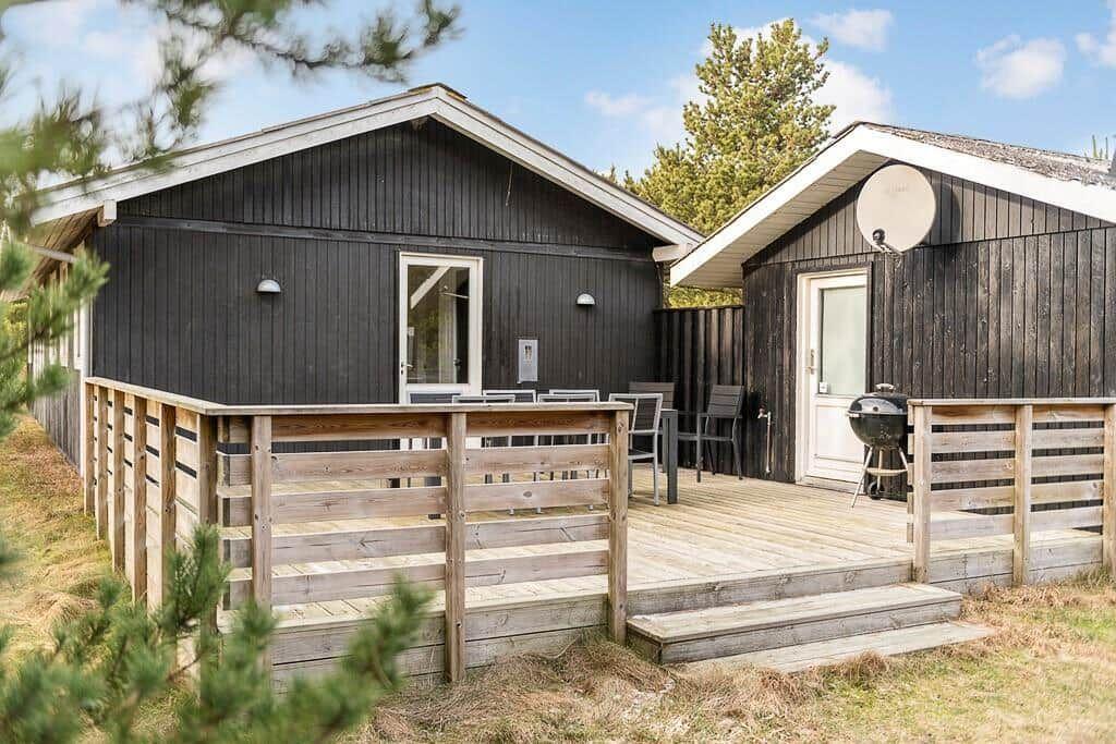 Zwei dunkelholzverkleidete Häuser mit Terrasse und Grill. Umgeben von Bäumen und Gras.