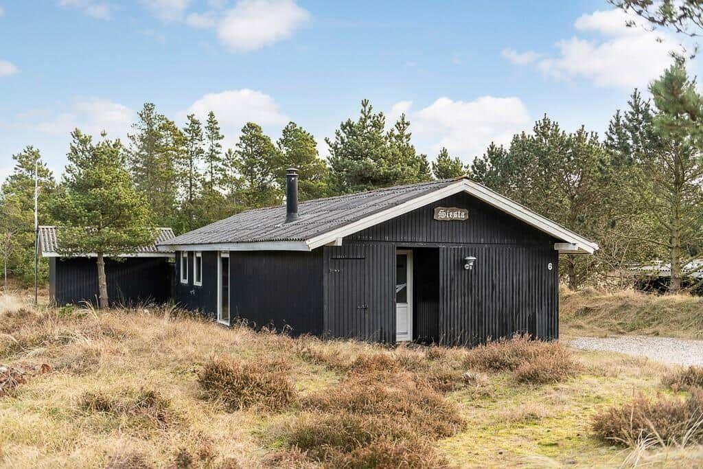 Schwarze Holzhütte mit Schornstein und Schild im Wald