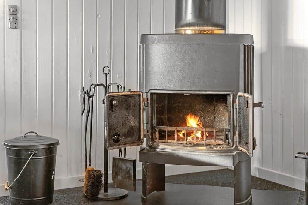Holzofen mit brennendem Feuer und Werkzeug neben einem Metallfass.