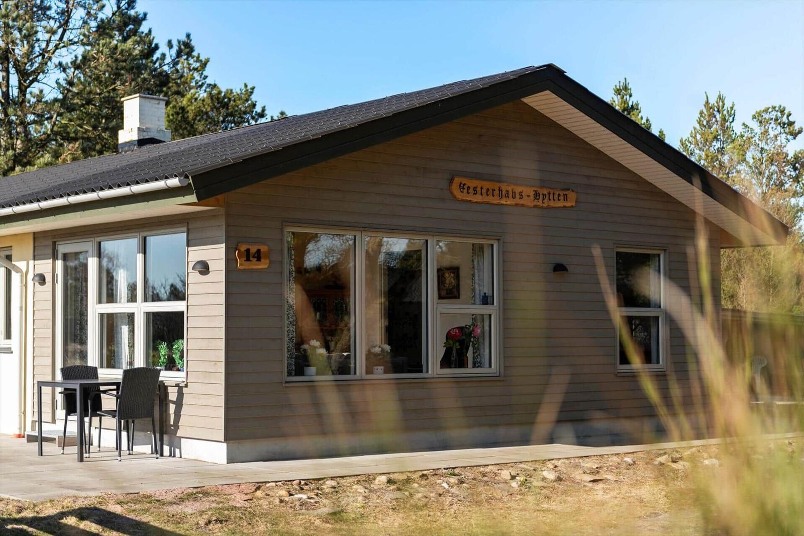 Haus mit Holzfassade, Terrasse und Garten. Nummer 14. Fenster zeigen Inneneinrichtung.