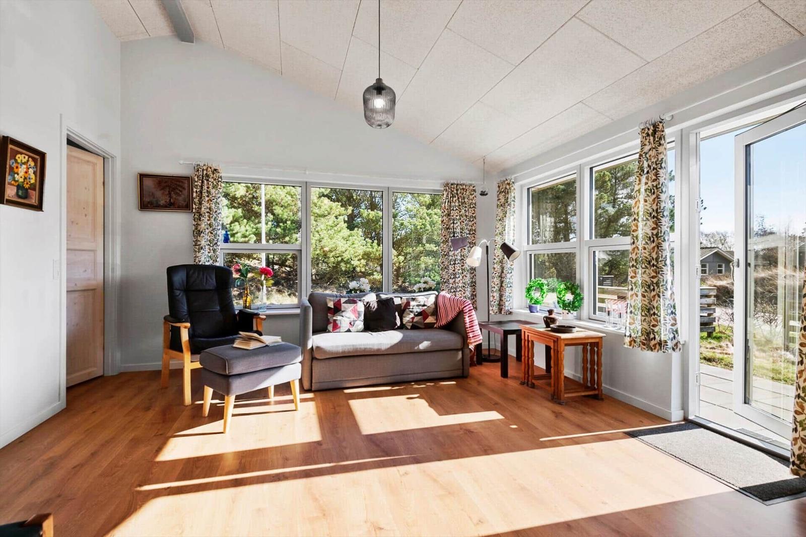 Wohnzimmer mit Sofa, Sessel und großen Fenstern. Holzboden und helle Wände.