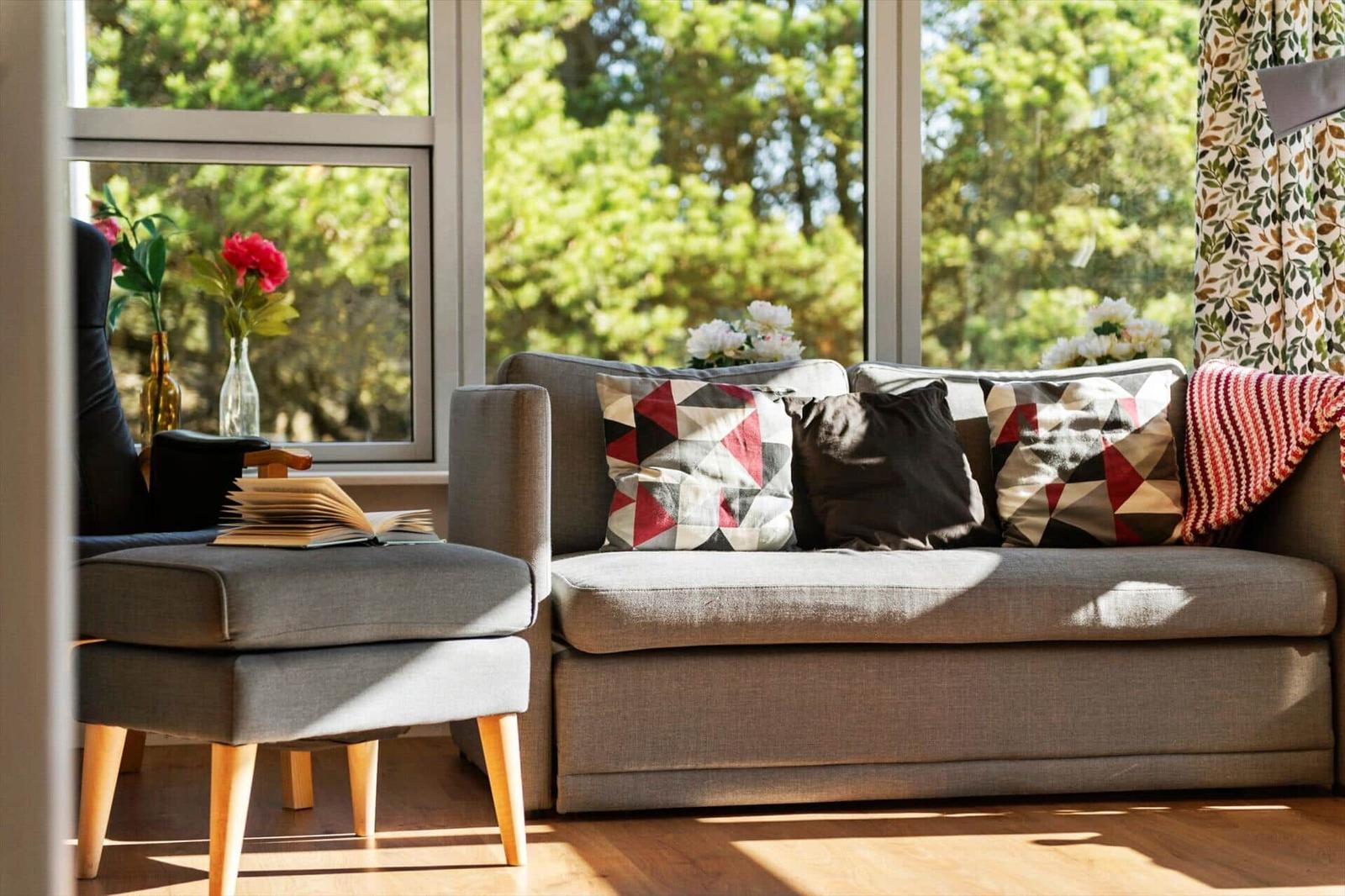 Ein grauer Sofa mit Kissen und einem Beistelltisch vor großen Fenstern.