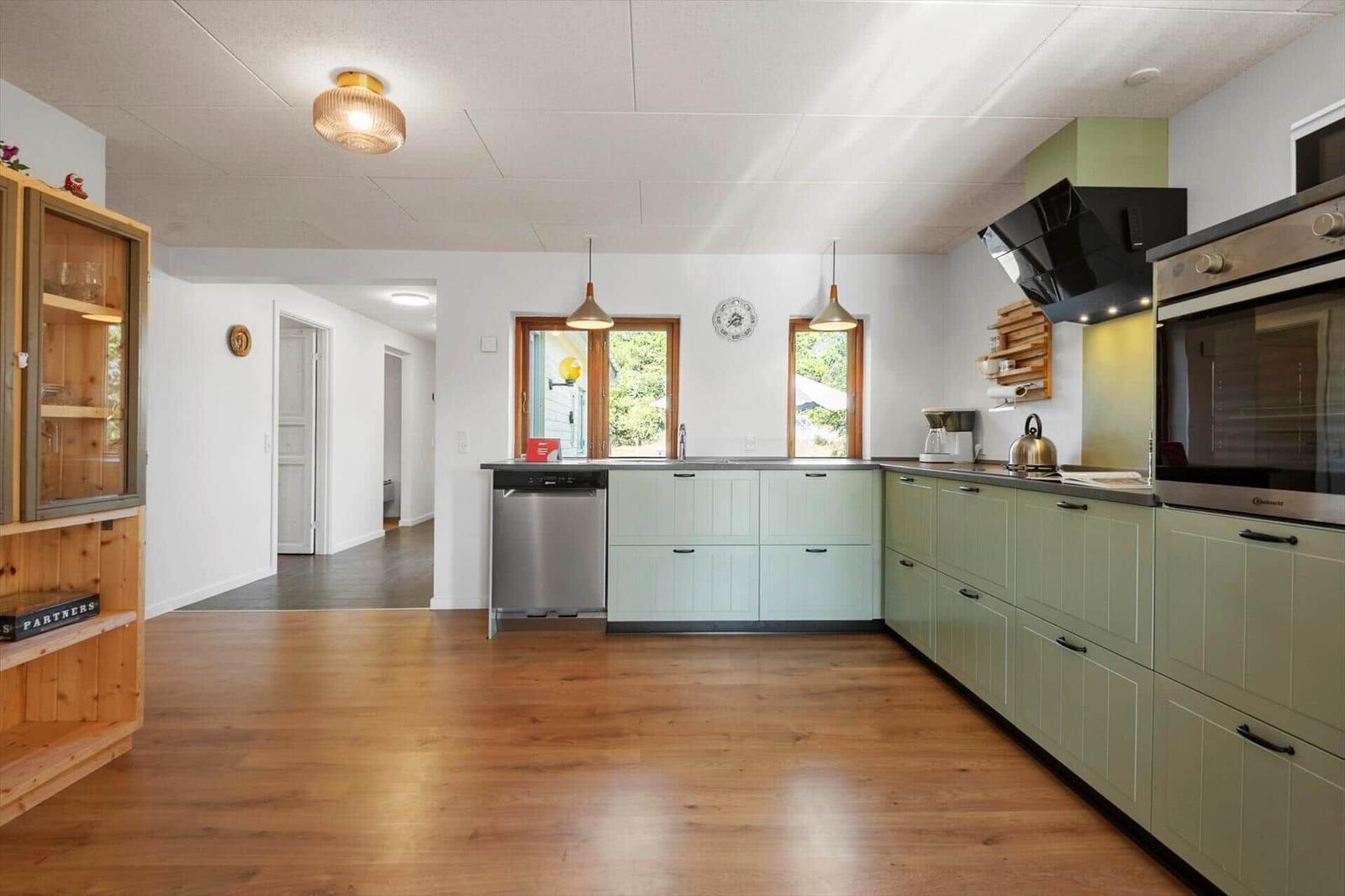 Küche mit grünen Schränken, Holzboden und Fenstern zum Garten