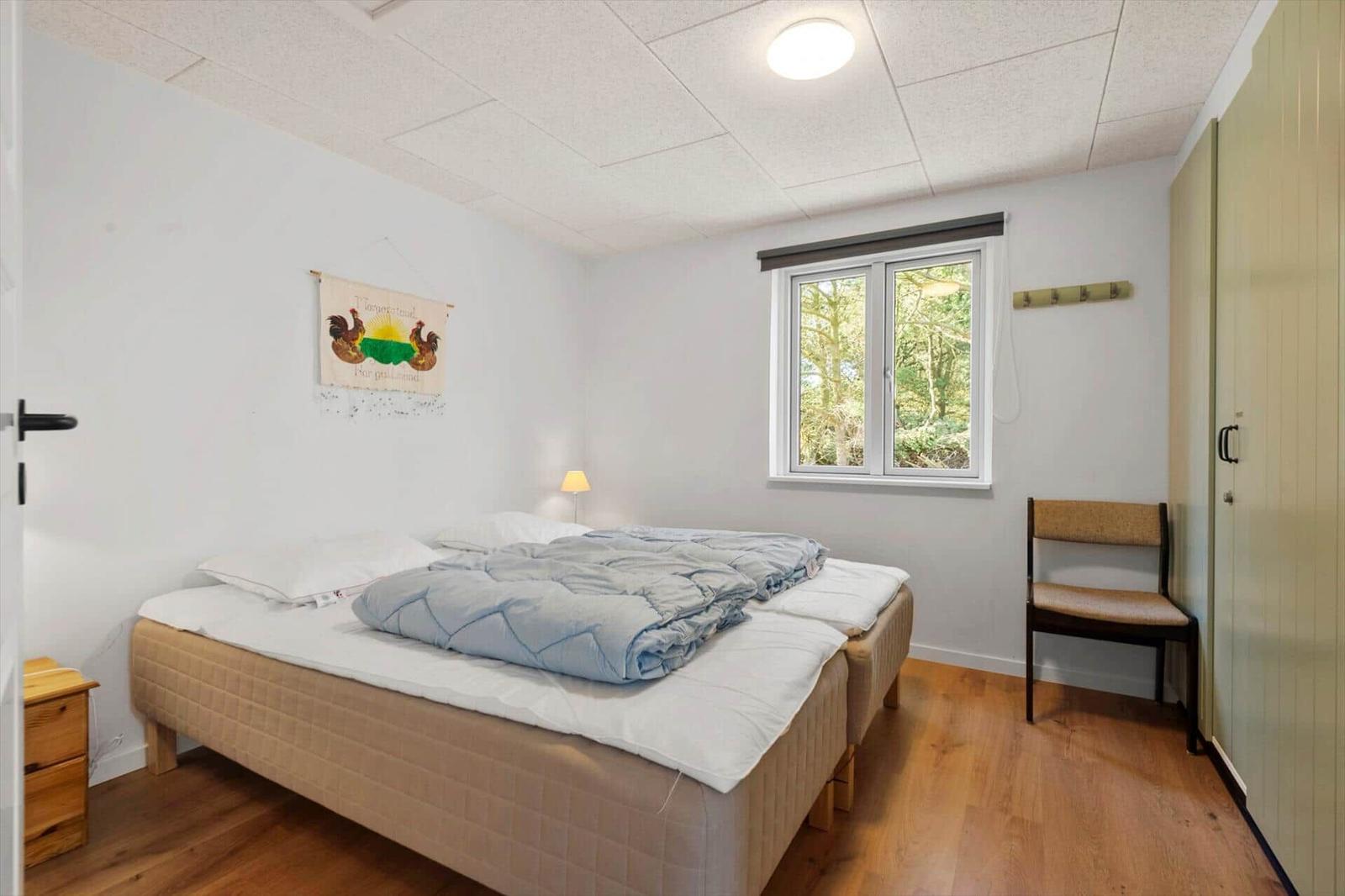 Schlafzimmer mit Bett, Fenster und Stuhl. Holzboden und Wanddekoration.