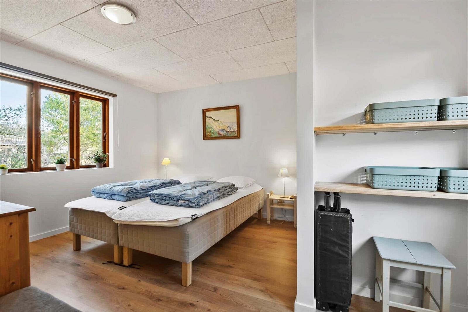 Schlafzimmer mit Doppelbett, Fenster und Regal mit Kisten.