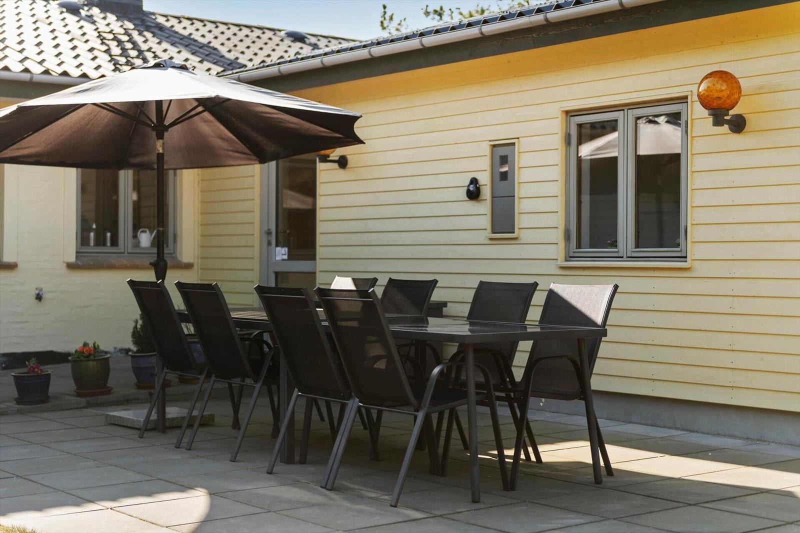 Terrasse mit Tisch, Stühlen und Sonnenschirm vor gelbem Haus
