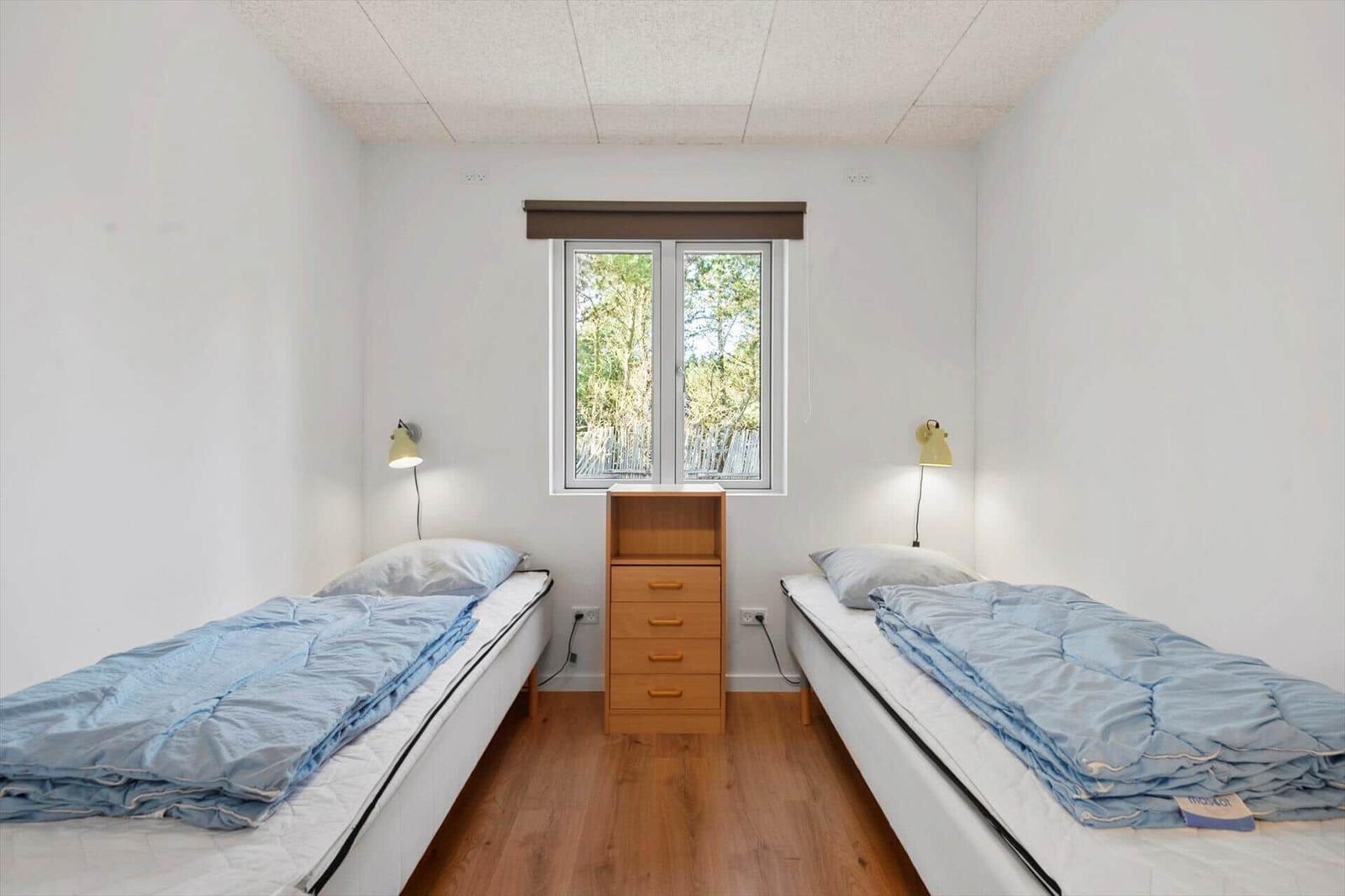 Zwei Einzelbetten mit blauen Decken, Holzschrank und Fenster mit Blick auf Bäume.