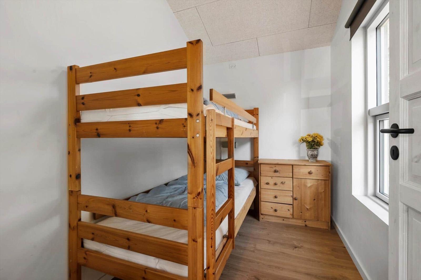 Ein Schlafzimmer mit einem Holzbett und einem Schrank. Ein Fenster und eine Tür sind sichtbar.