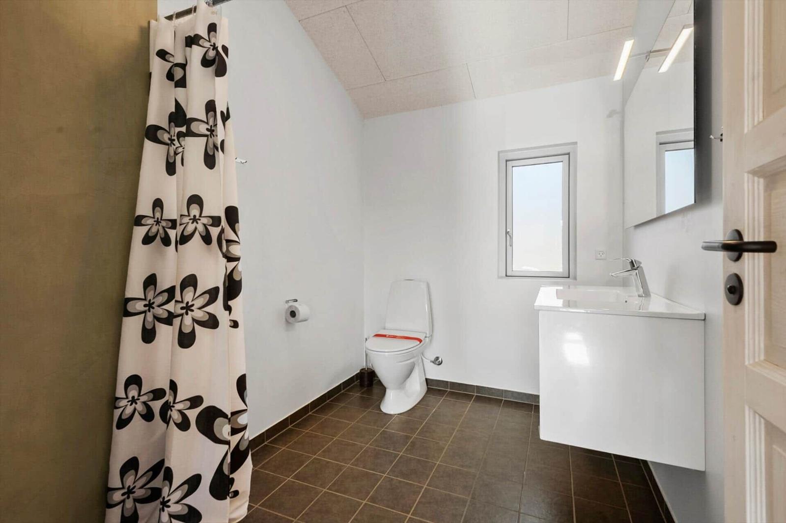 Badezimmer mit Toilette, Waschbecken und Dusche mit floraler Plane.