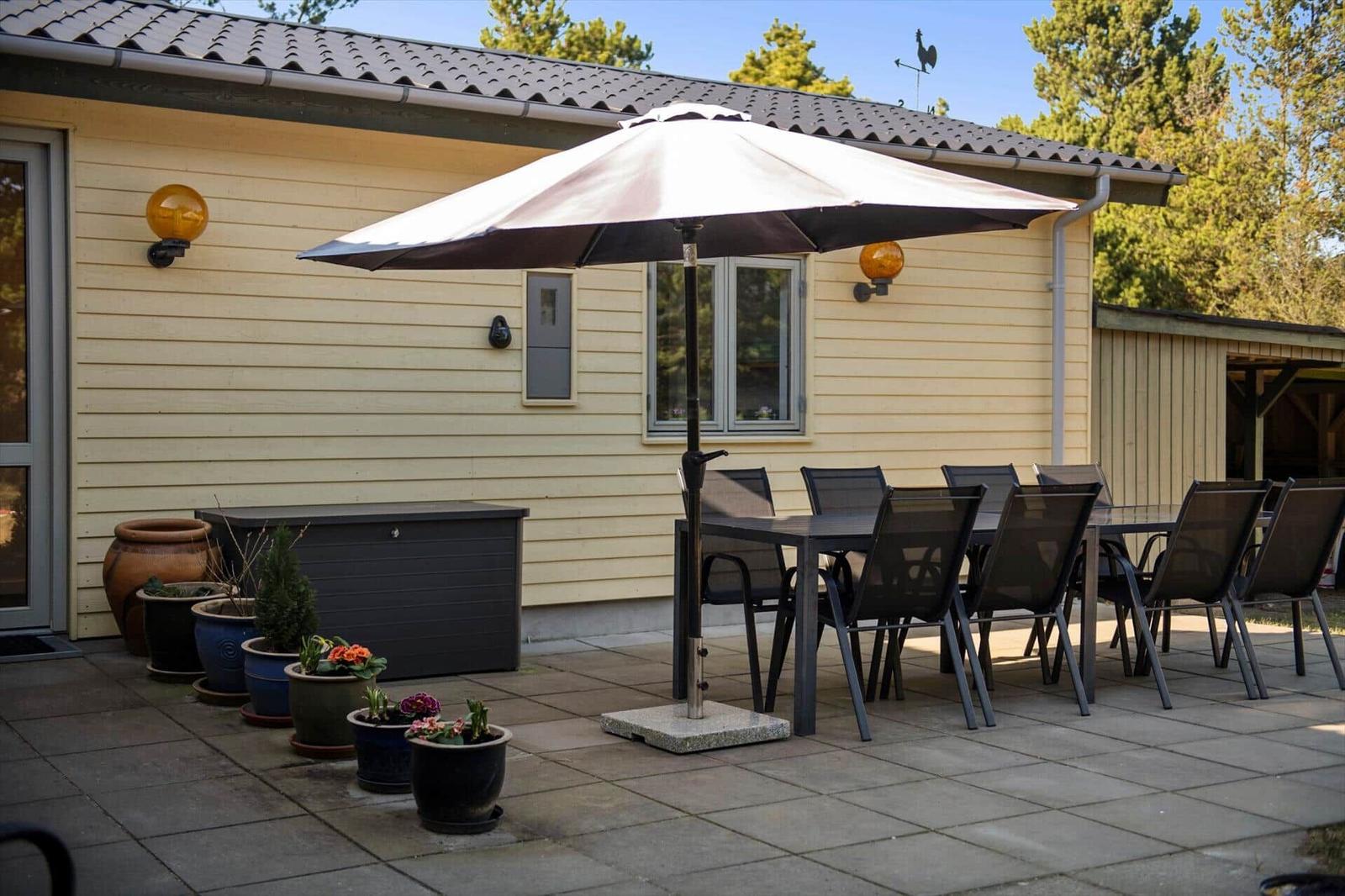 Terrasse mit Tisch, Stühlen und Sonnenschirm vor einem Haus