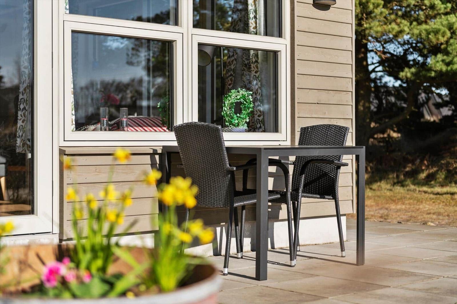 Terrasse mit Tisch und zwei Stühlen vor einem Haus mit Fenster.