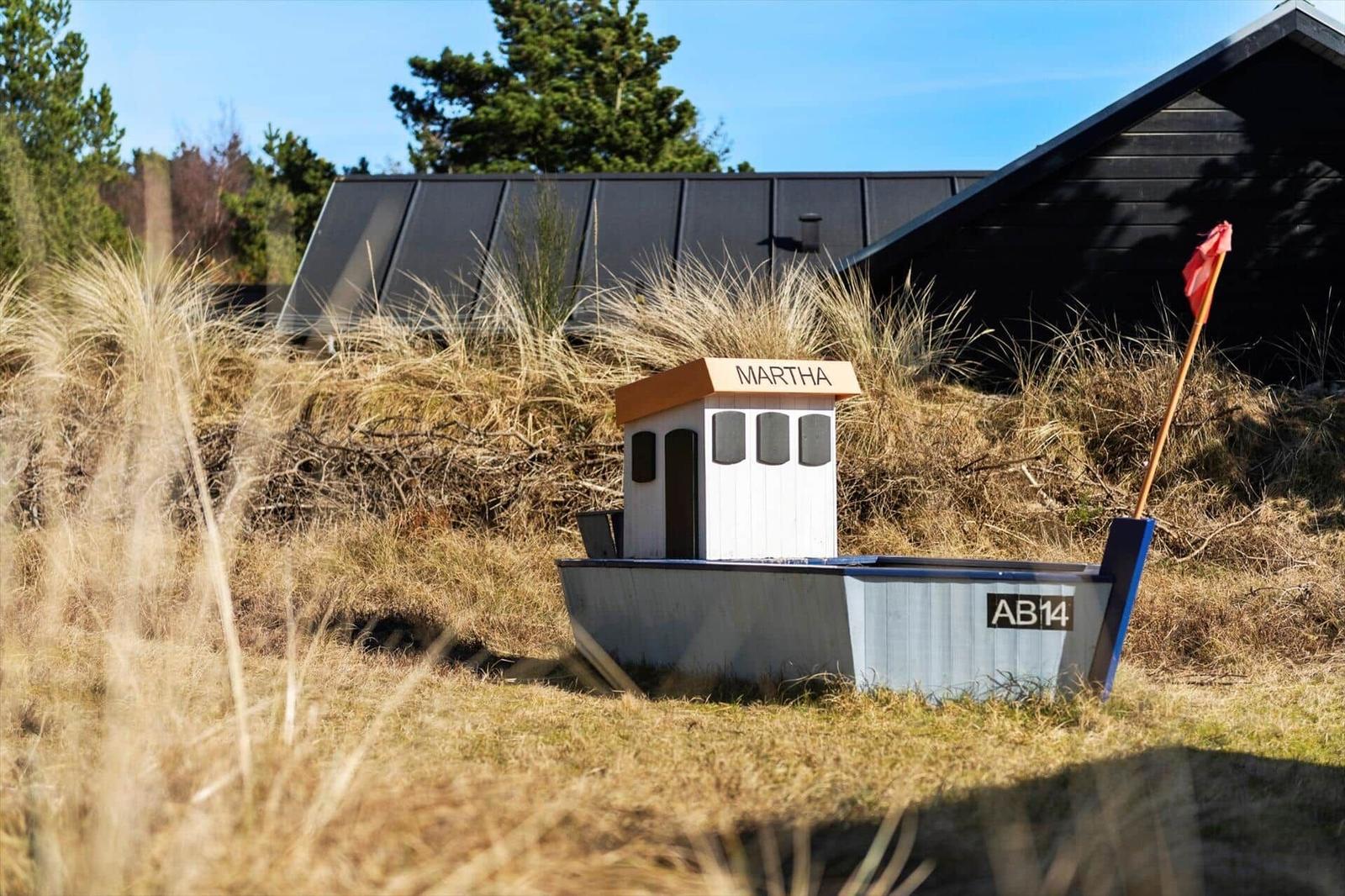 Ein kleines Boot namens Martha steht vor einem schwarzen Haus auf Gras.