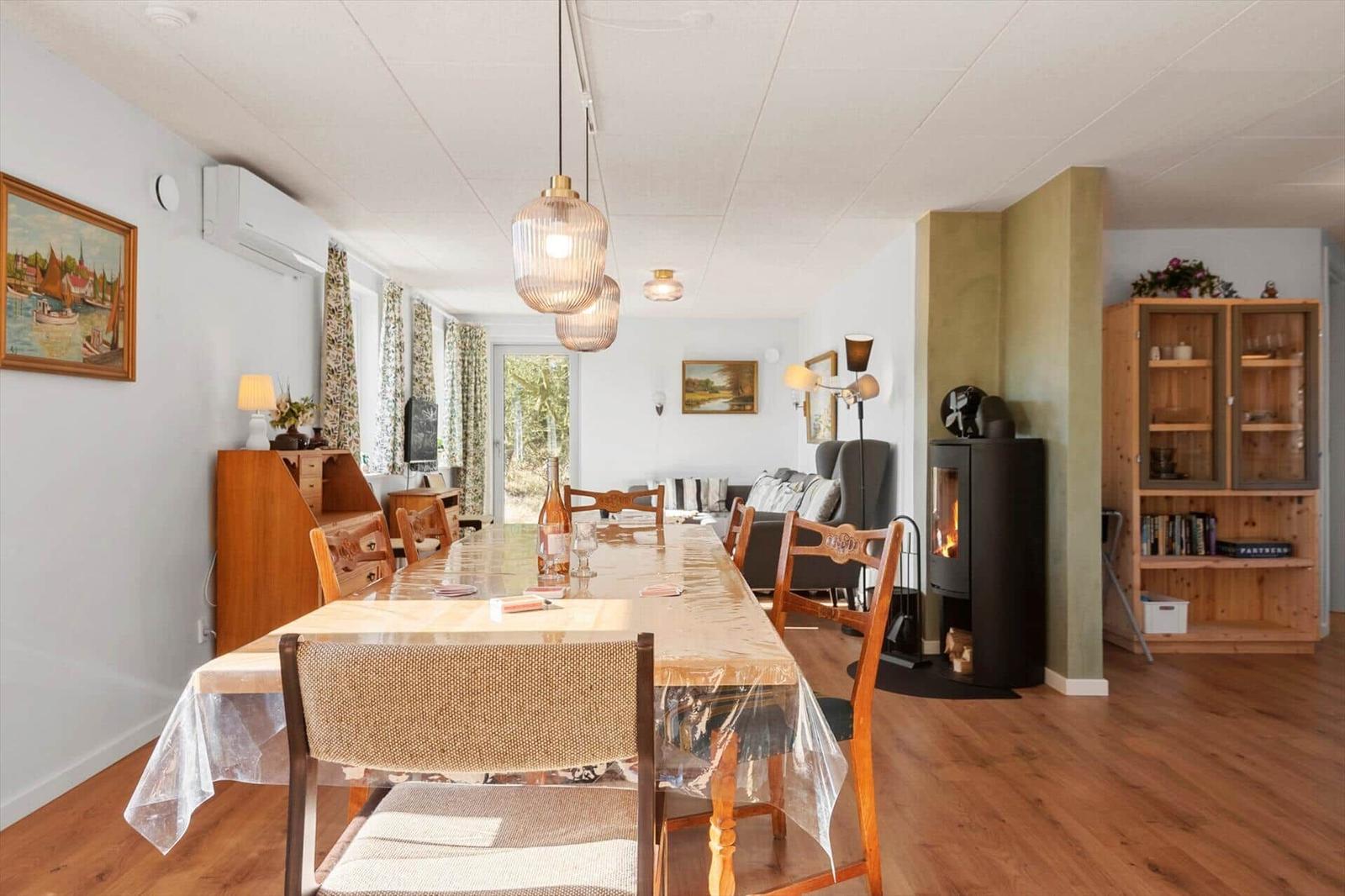 Esszimmer mit Esstisch, Stühlen und Kaminofen. Wohnbereich mit Sofa und Bücherregal.