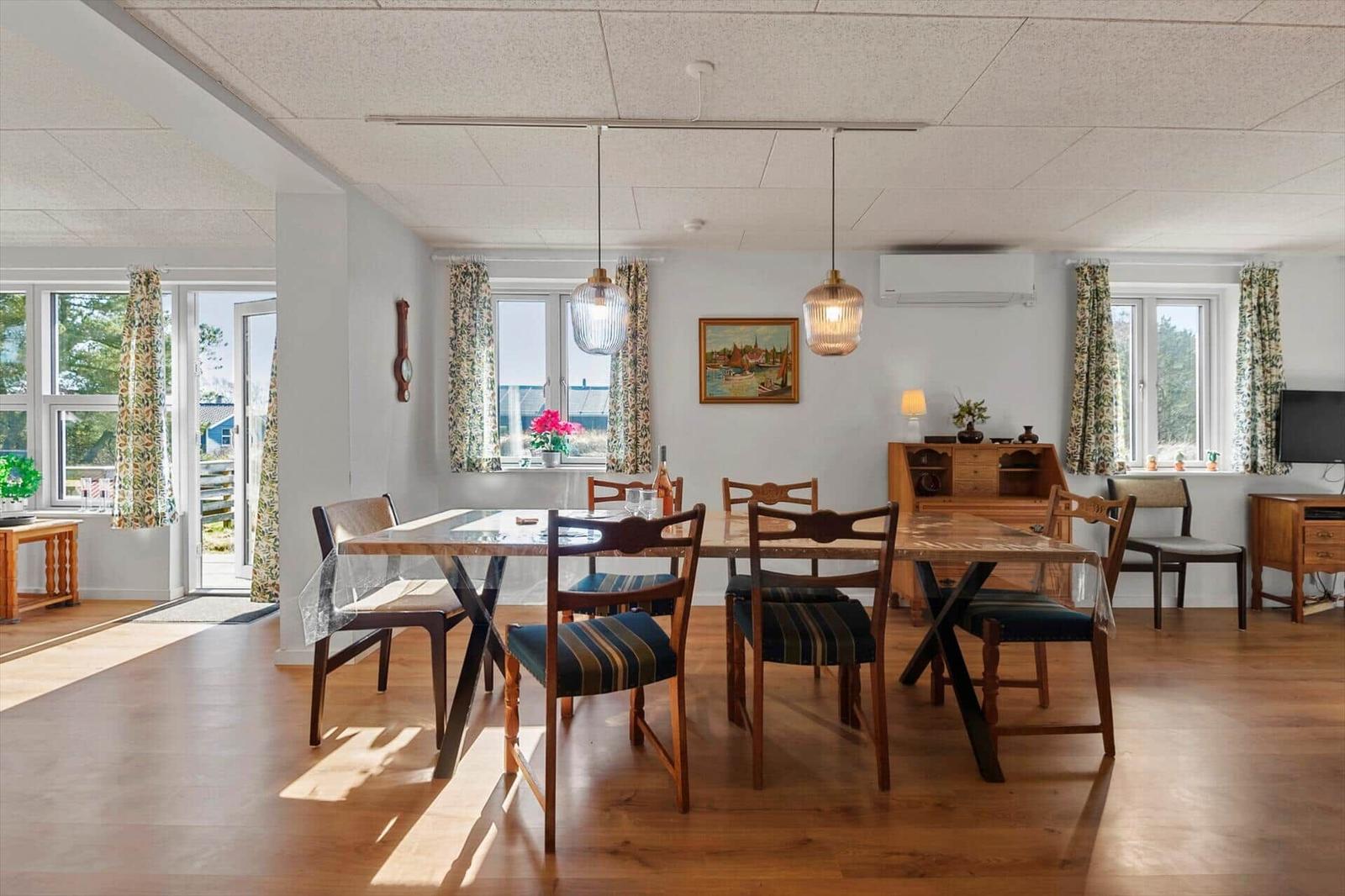 Esszimmer mit Holztisch, Stühlen und Fenstern mit Vorhängen.