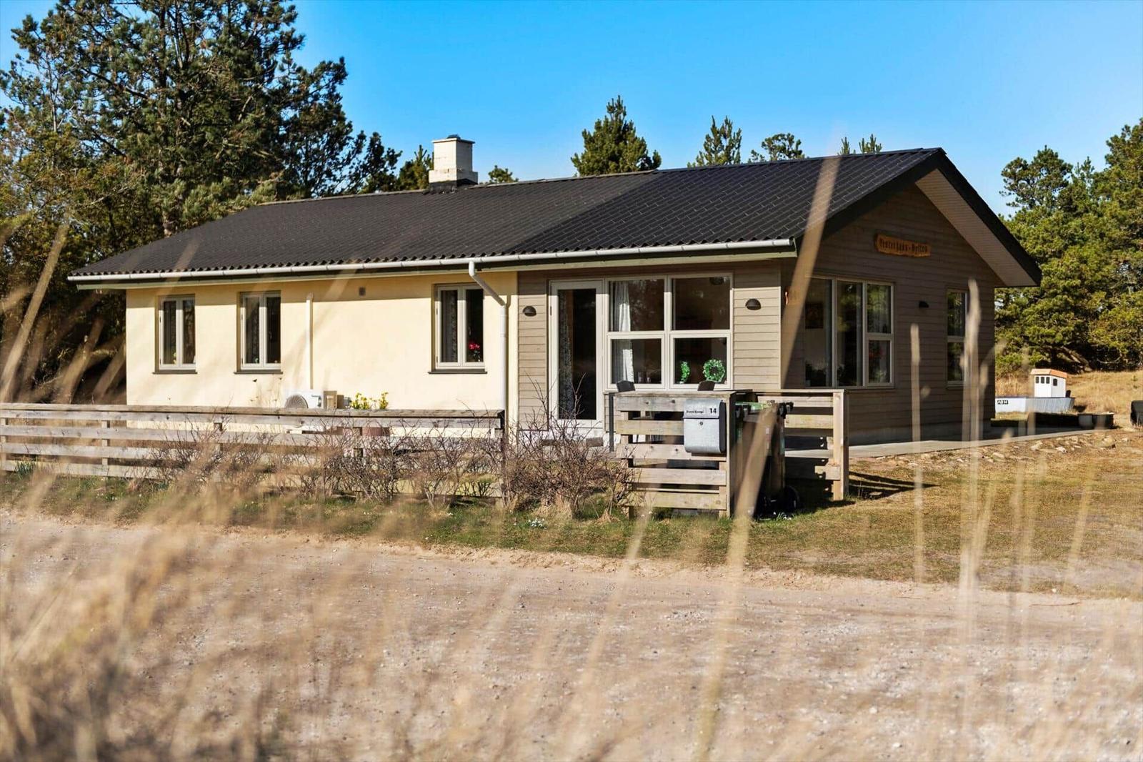 Ein kleines Haus mit dunklem Dach und Holzveranda. Umgeben von Bäumen und Gras.