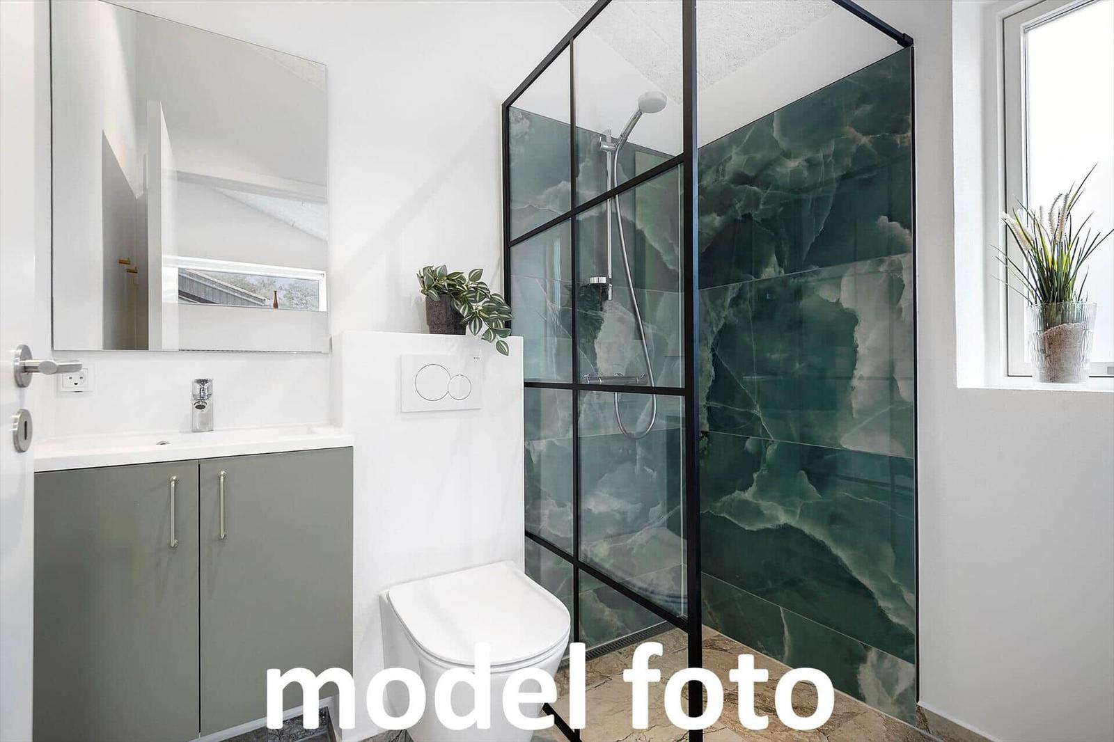 Badezimmer mit Dusche, Toilette und Waschbecken. Grüne Marmorwand und Fenster mit Pflanze.