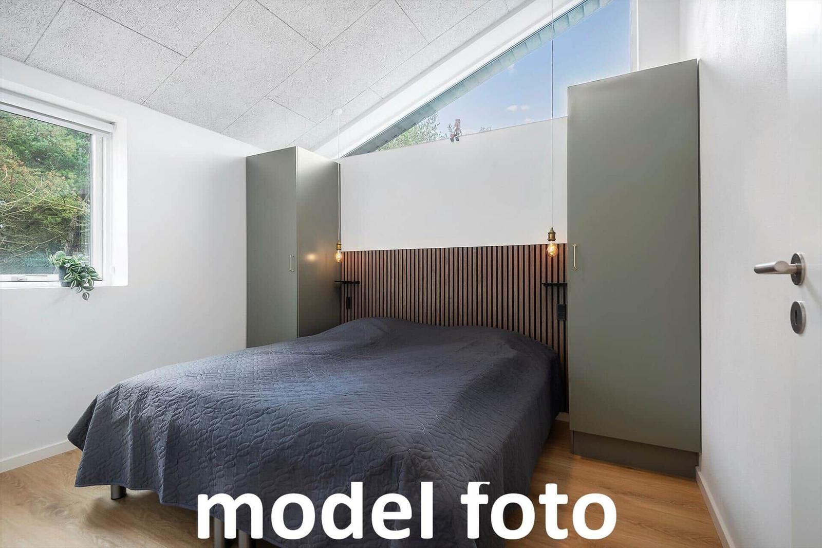 Schlafzimmer mit Doppelbett, Holzfußboden und großem Fenster. Zwei Schränke und Holzpaneel an der Wand.