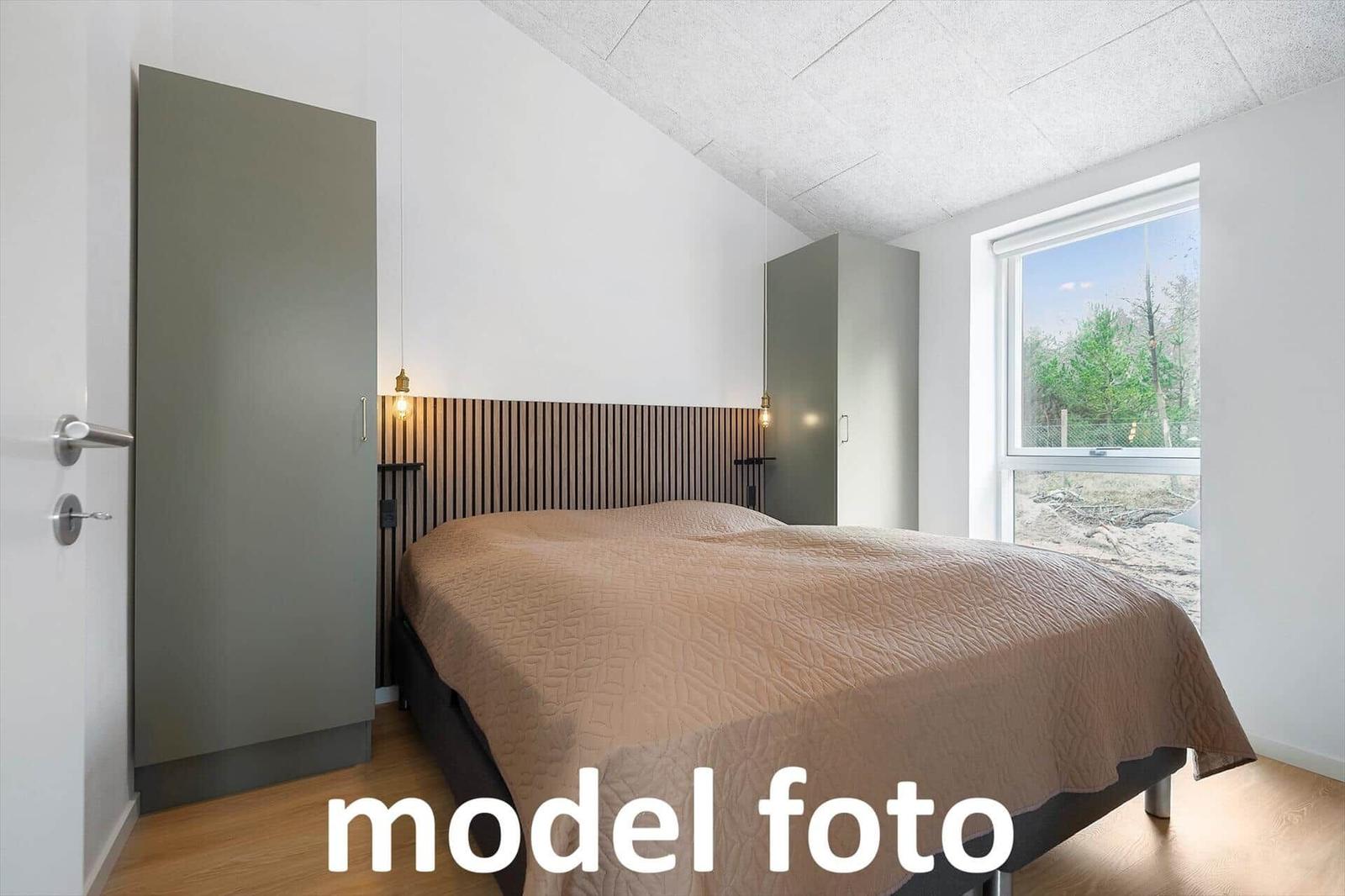 Schlafzimmer mit Bett, Kleiderschrank und Fensterblick auf Wald.
