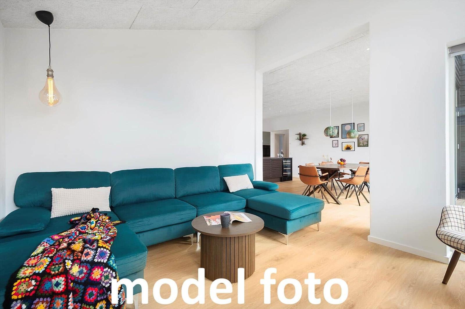Ein Wohnzimmer mit türkisfarbenem Sofa, Holzboden und Essbereich im Hintergrund.