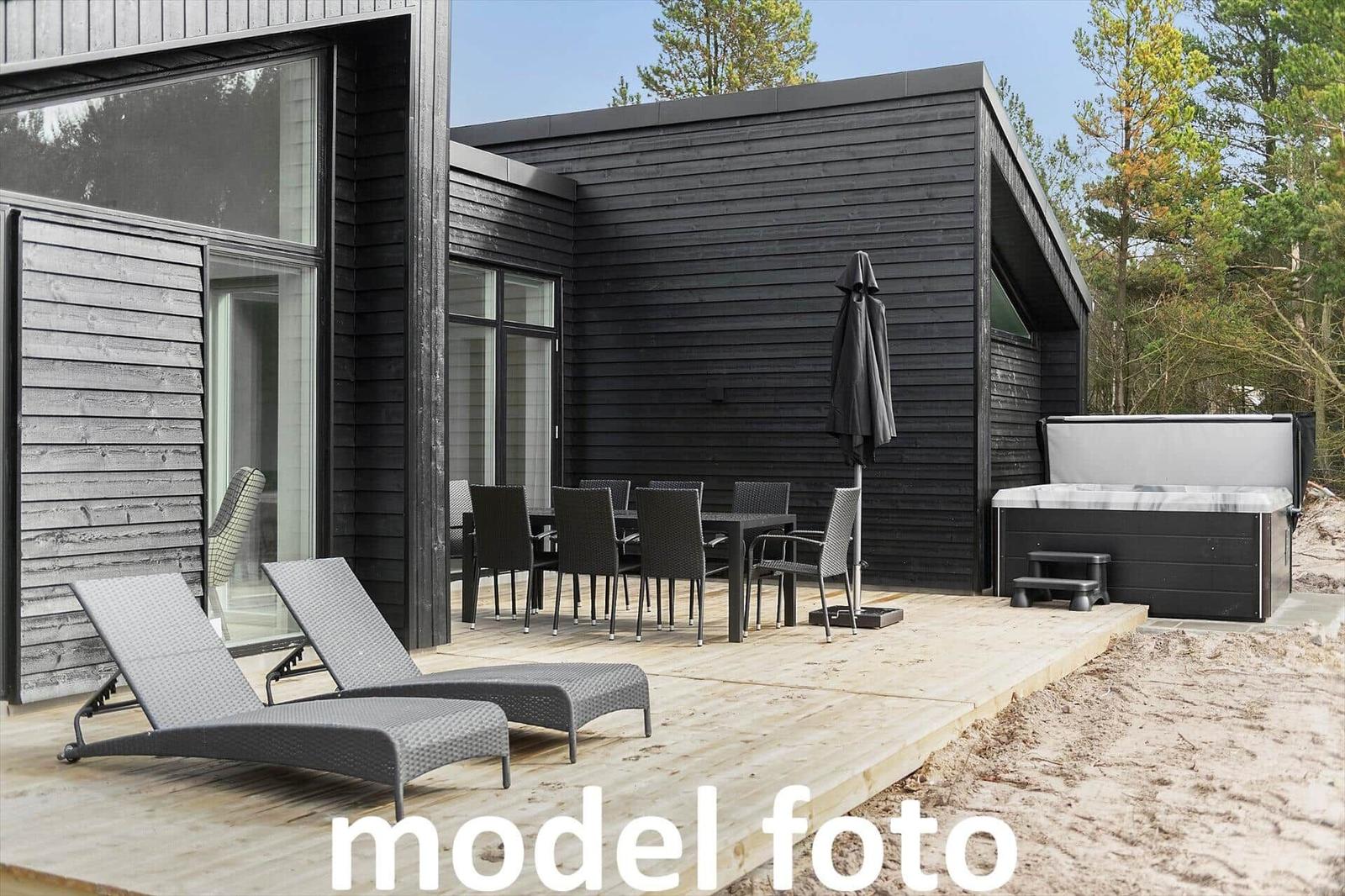 Terrasse mit Liegen, Tisch, Stühlen und Whirlpool neben modernem Holzhaus.