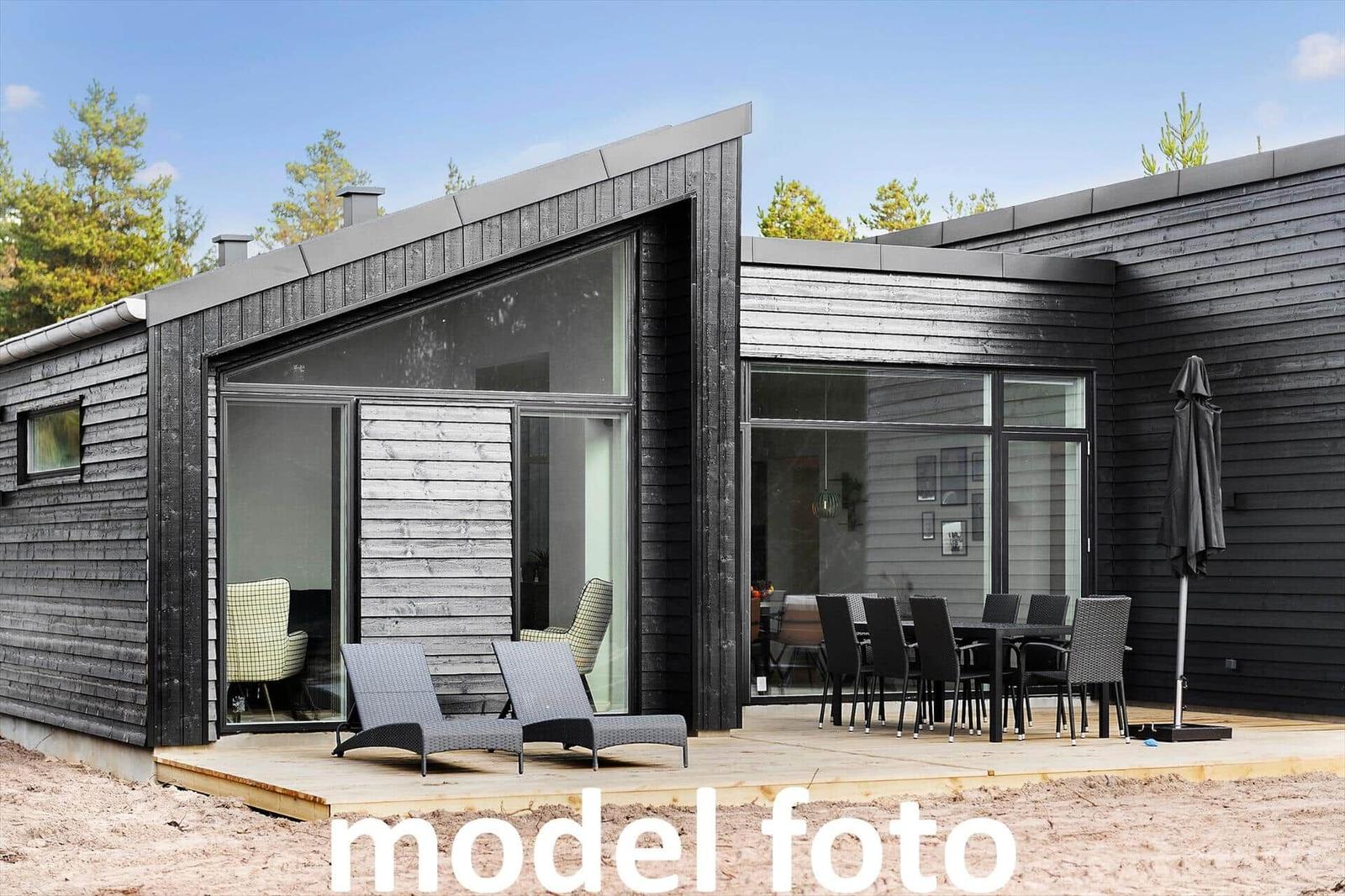 Moderne Holzhütte mit Terrasse, Liegen und Esstisch. Blick in Wohn- und Essbereich.