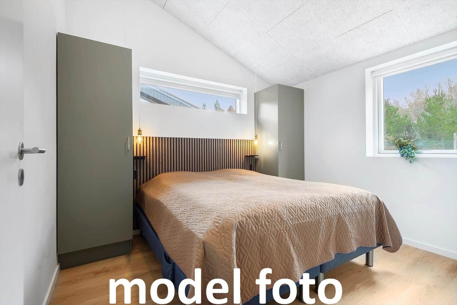 Schlafzimmer mit Bett, Kleiderschrank und Fenstern.