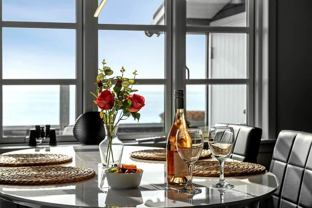 Runder Tisch mit Wein, Blumen und Meerblick durch Fenster