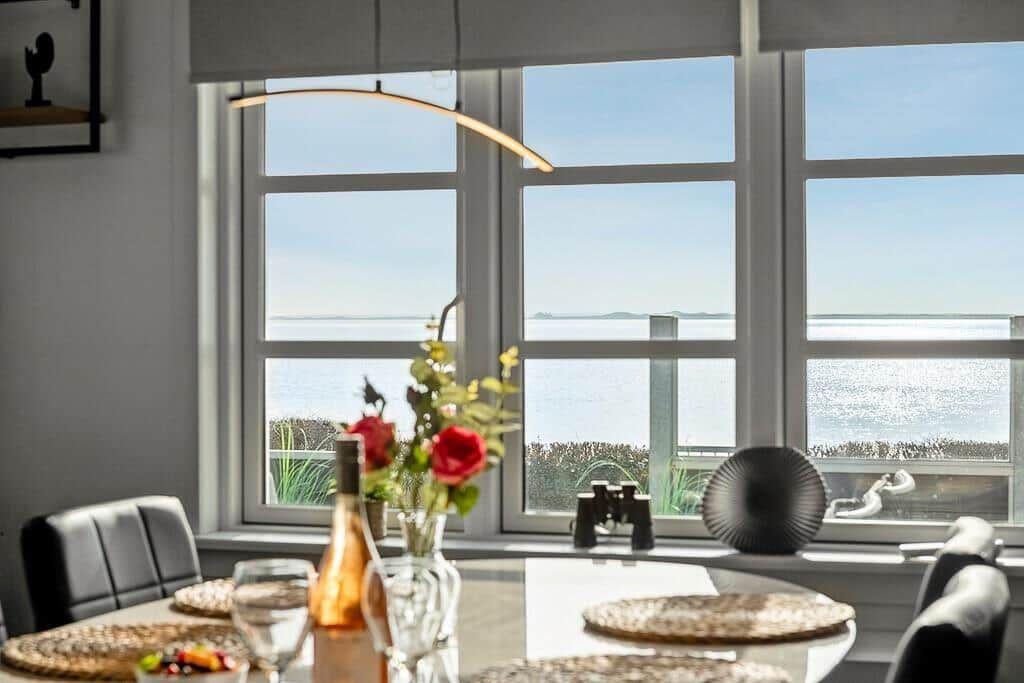 Essbereich mit Meerblick durch große Fenster und Tischdekoration.