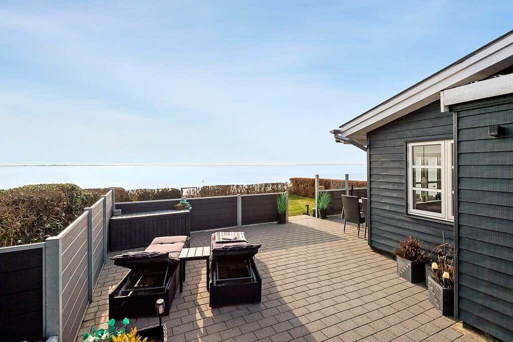 Terrasse mit Loungemöbeln und Meerblick. Holzwand und Fenster sichtbar.