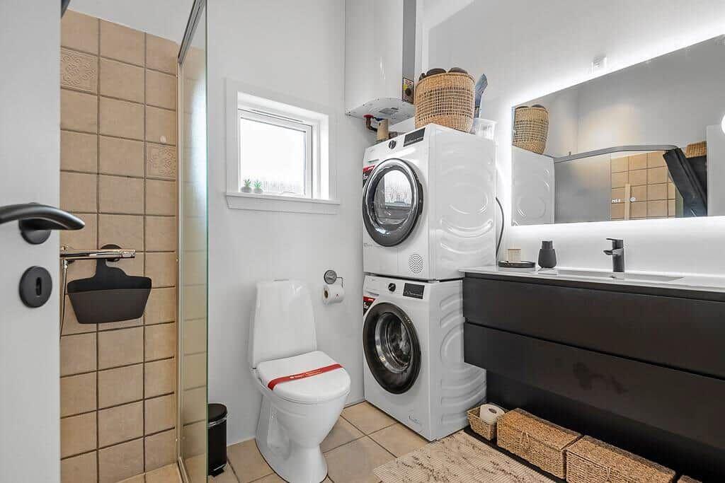 Badezimmer mit Dusche, Toilette, Waschmaschine und Spiegelschrank.
