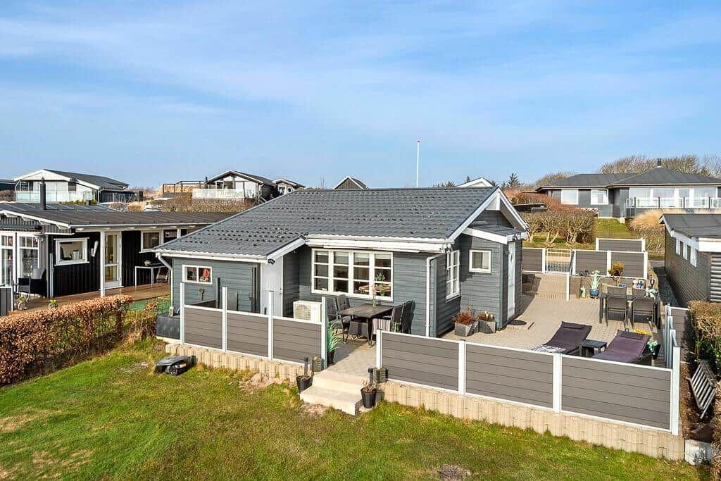 Ein graues Ferienhaus mit Terrasse und Garten. Möbel und Pflanzen sind draußen platziert.