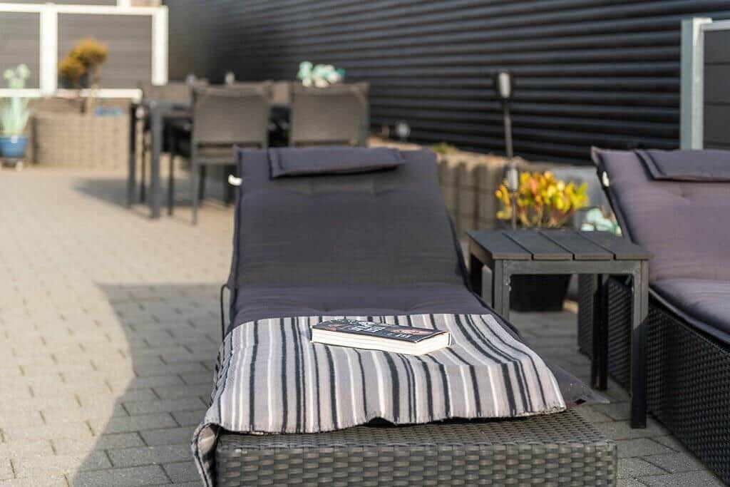 Terrasse mit Liegen, Tisch und Pflanzen. Buch liegt auf einer Decke.