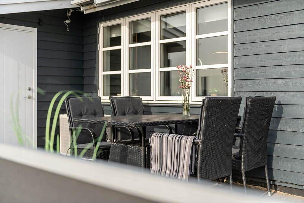 Terrasse mit Tisch und Stühlen vor grauem Haus mit Fenster.