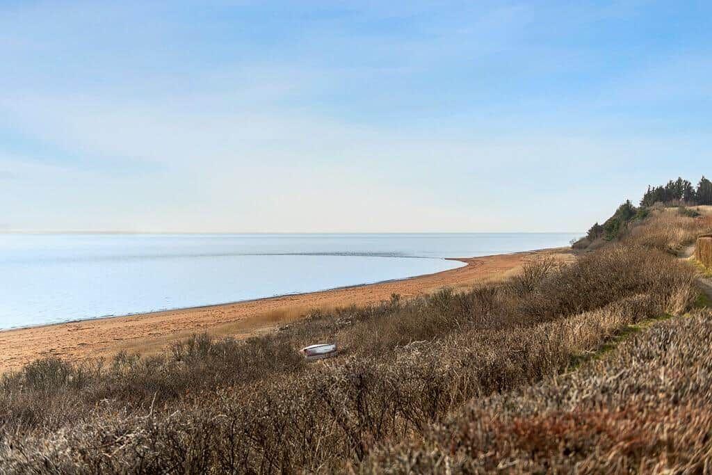 Strand mit sandigem Ufer und ruhigem Meer unter blauem Himmel.