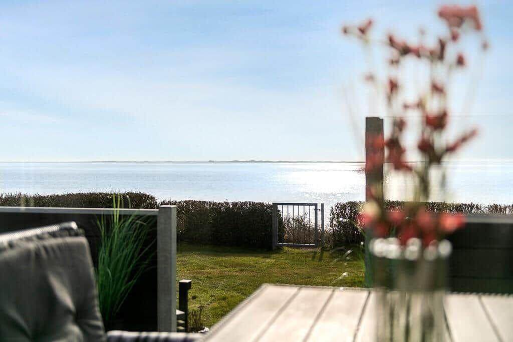 Terrasse mit Blick auf ruhiges Wasser und grünen Rasenbereich.