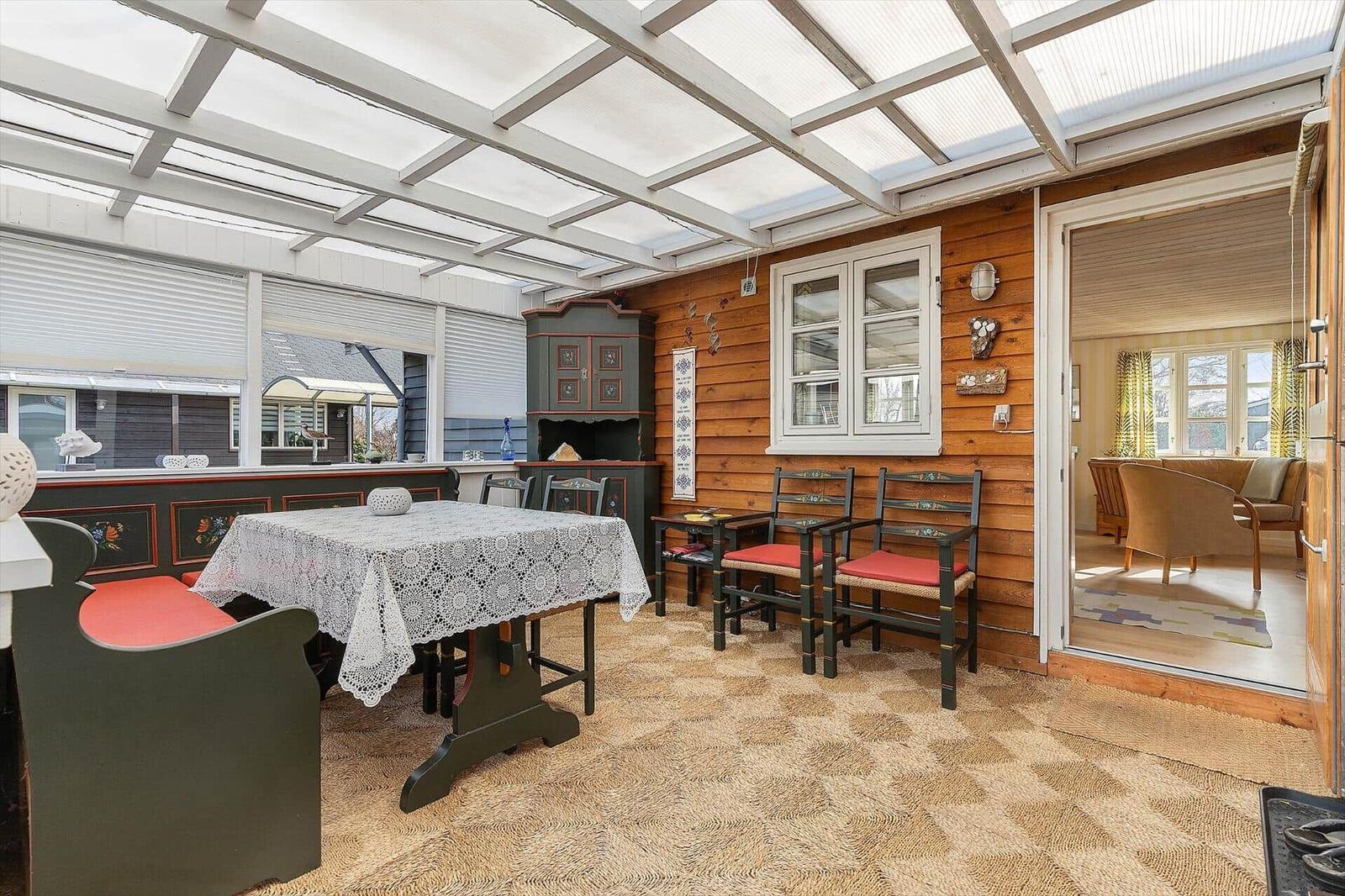 Terrassenbereich mit Tisch, Stühlen und Holzwand. Durchgang zu Wohnraum.