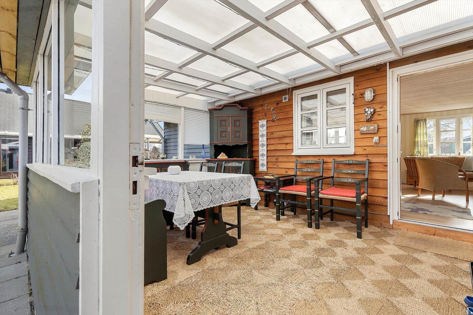 Terrasse mit Tisch, Stühlen und Holzwand. Durchgang ins Wohnzimmer.