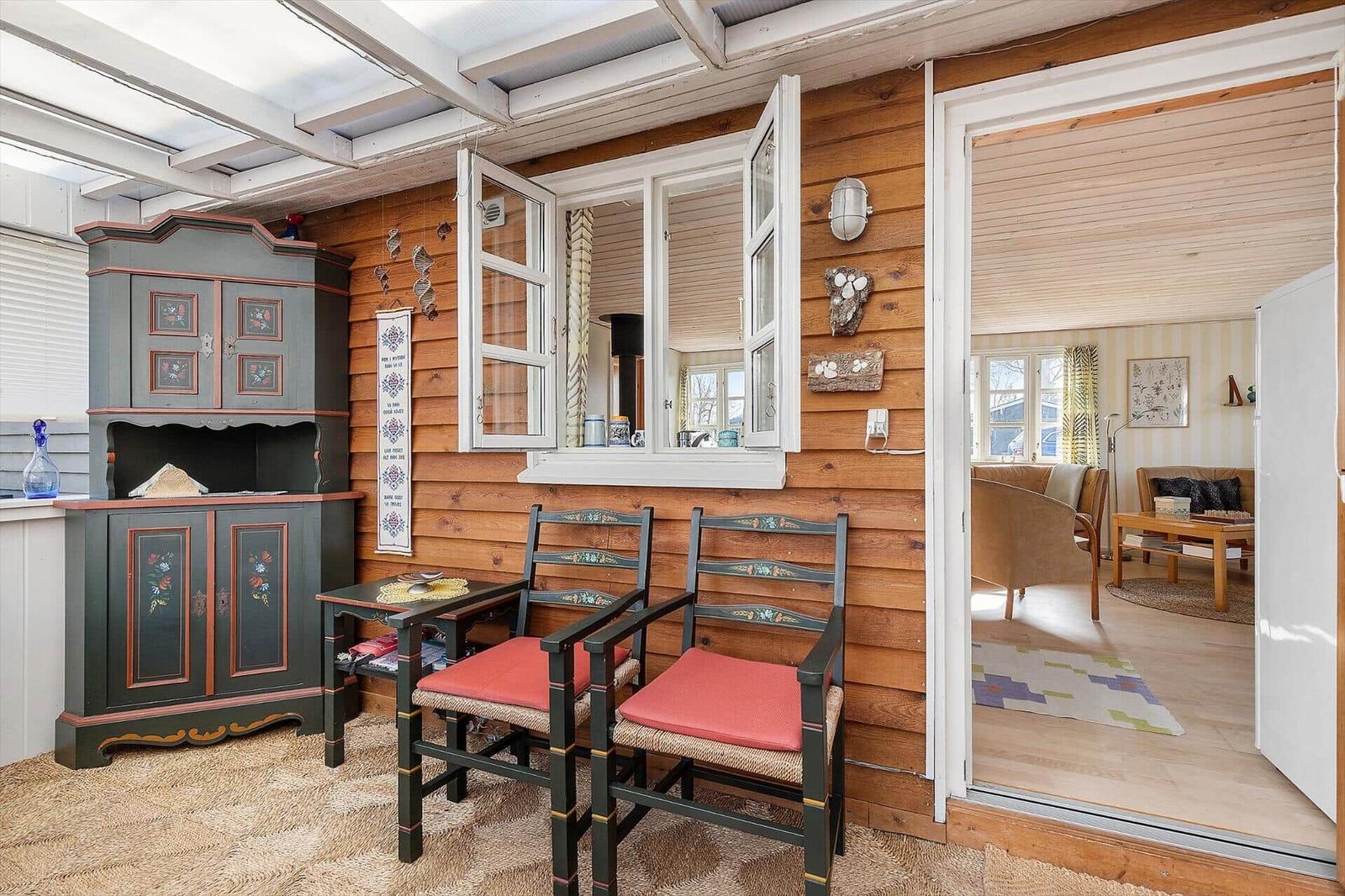 Terrasse mit Holzwand, zwei Stühlen und einem Schrank. Durchgang in Wohnzimmer mit Sofa.