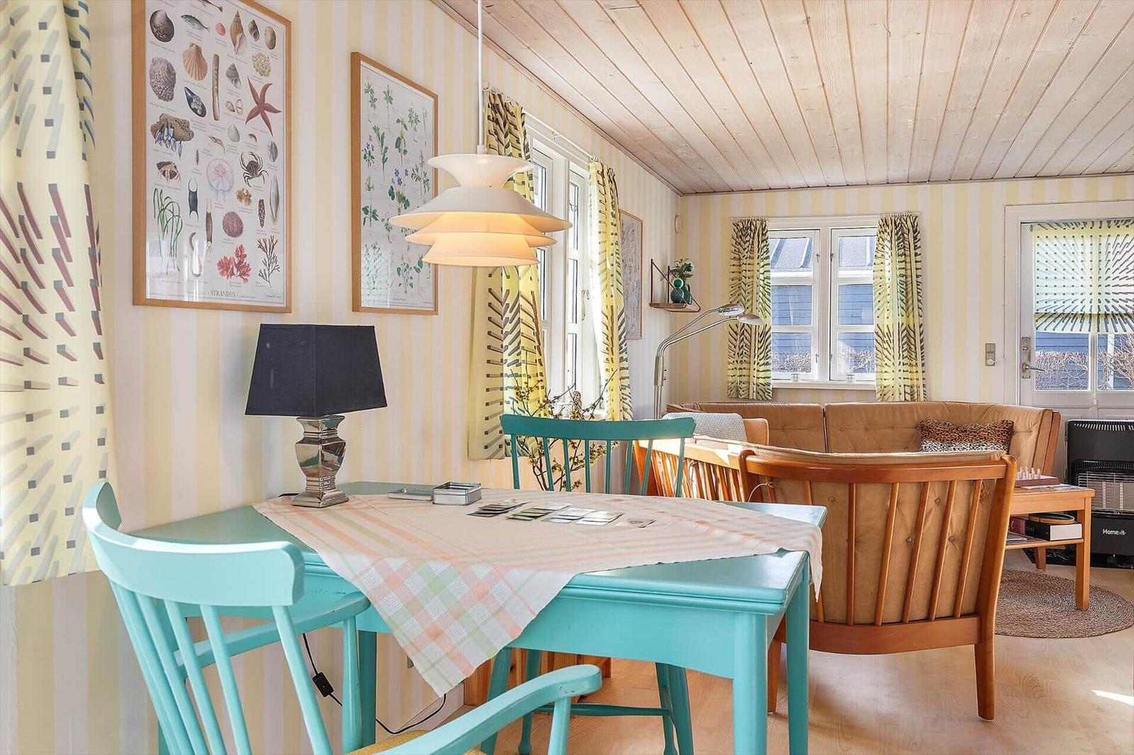 Esszimmer mit Tisch, Stühlen und Wandbildern. Sofa und Fenster im Hintergrund.