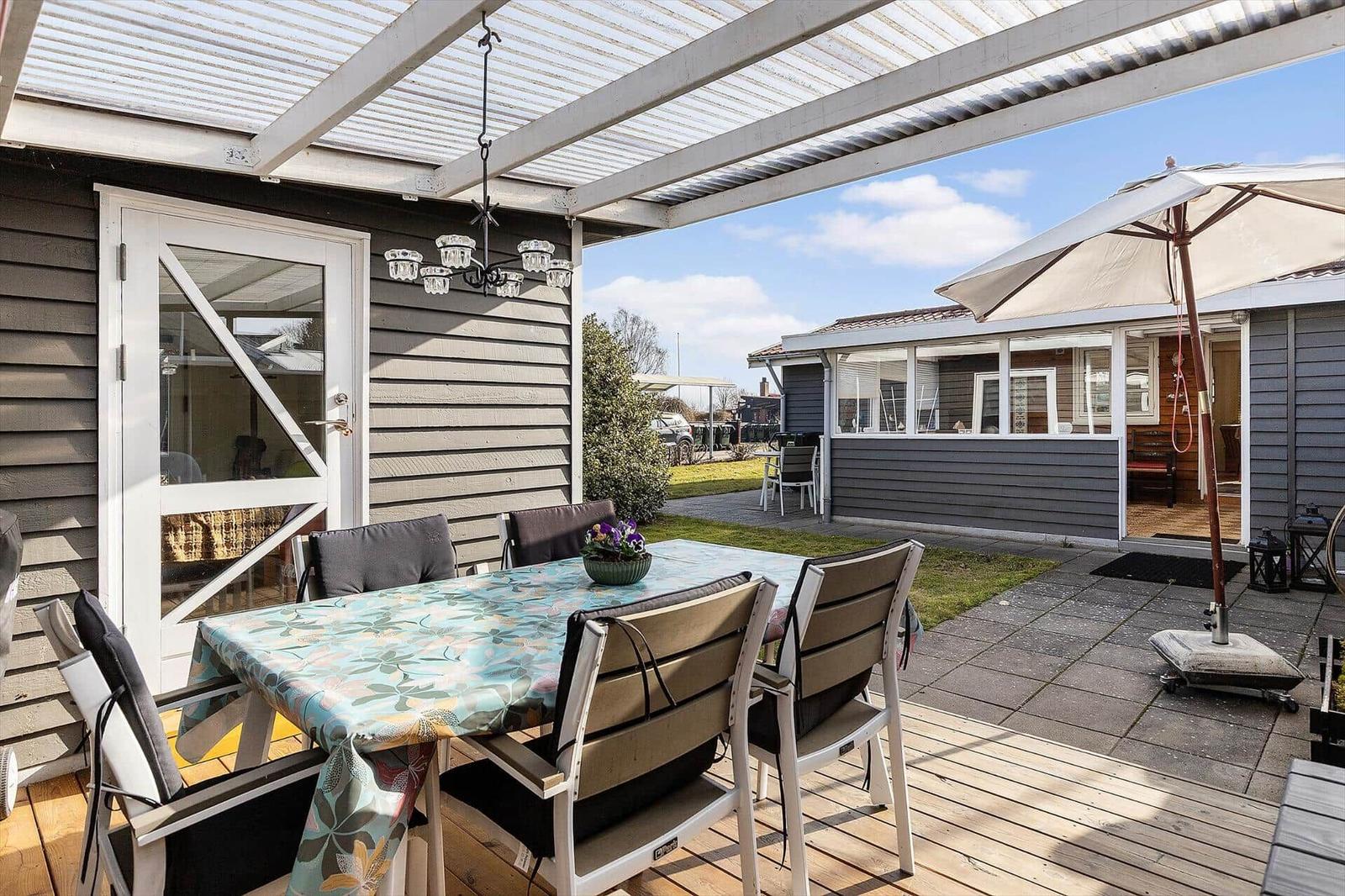 Terrasse mit Tisch, Stühlen und Sonnenschutz. Hintergrund zeigt Wohnhaus mit Fenstern.