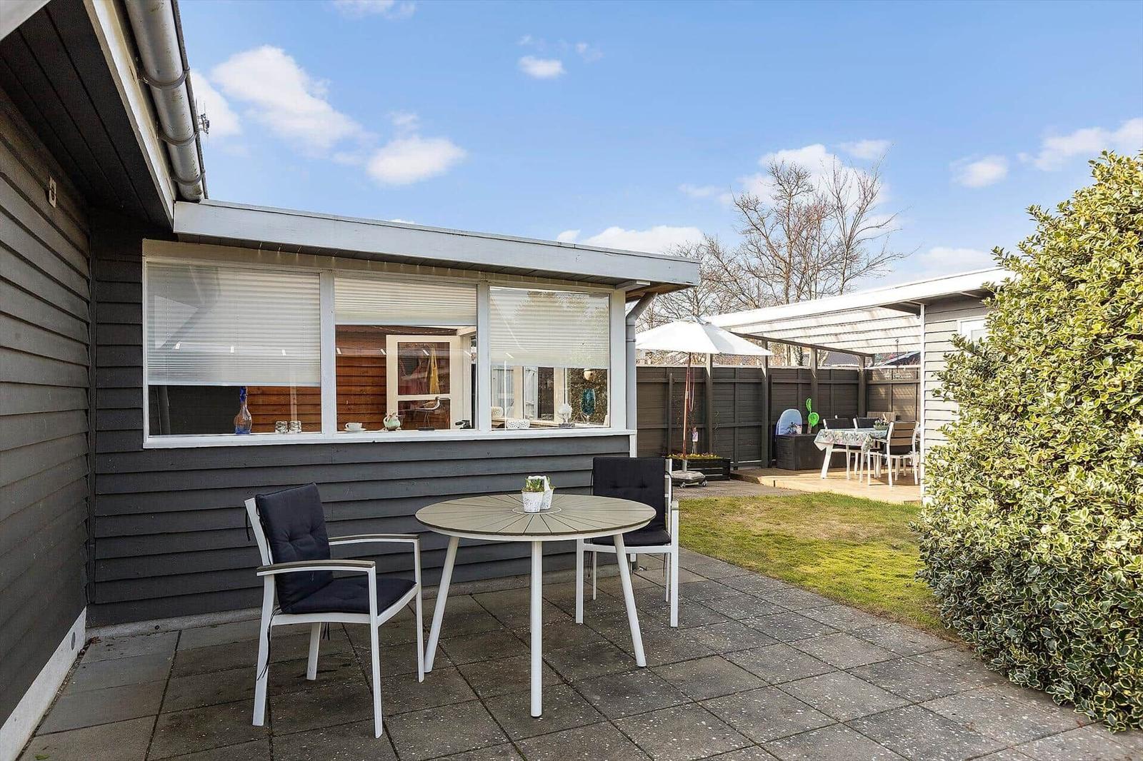 Terrasse mit Tisch und Stühlen, Gartenbereich mit Sonnenschirm und Grillplatz.