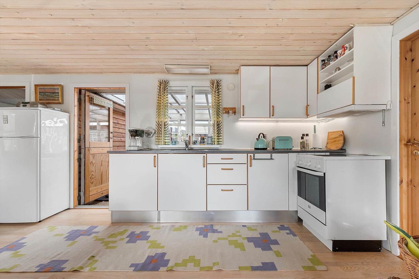 Küche mit weißen Schränken, Holzdecke und gemustertem Teppich.