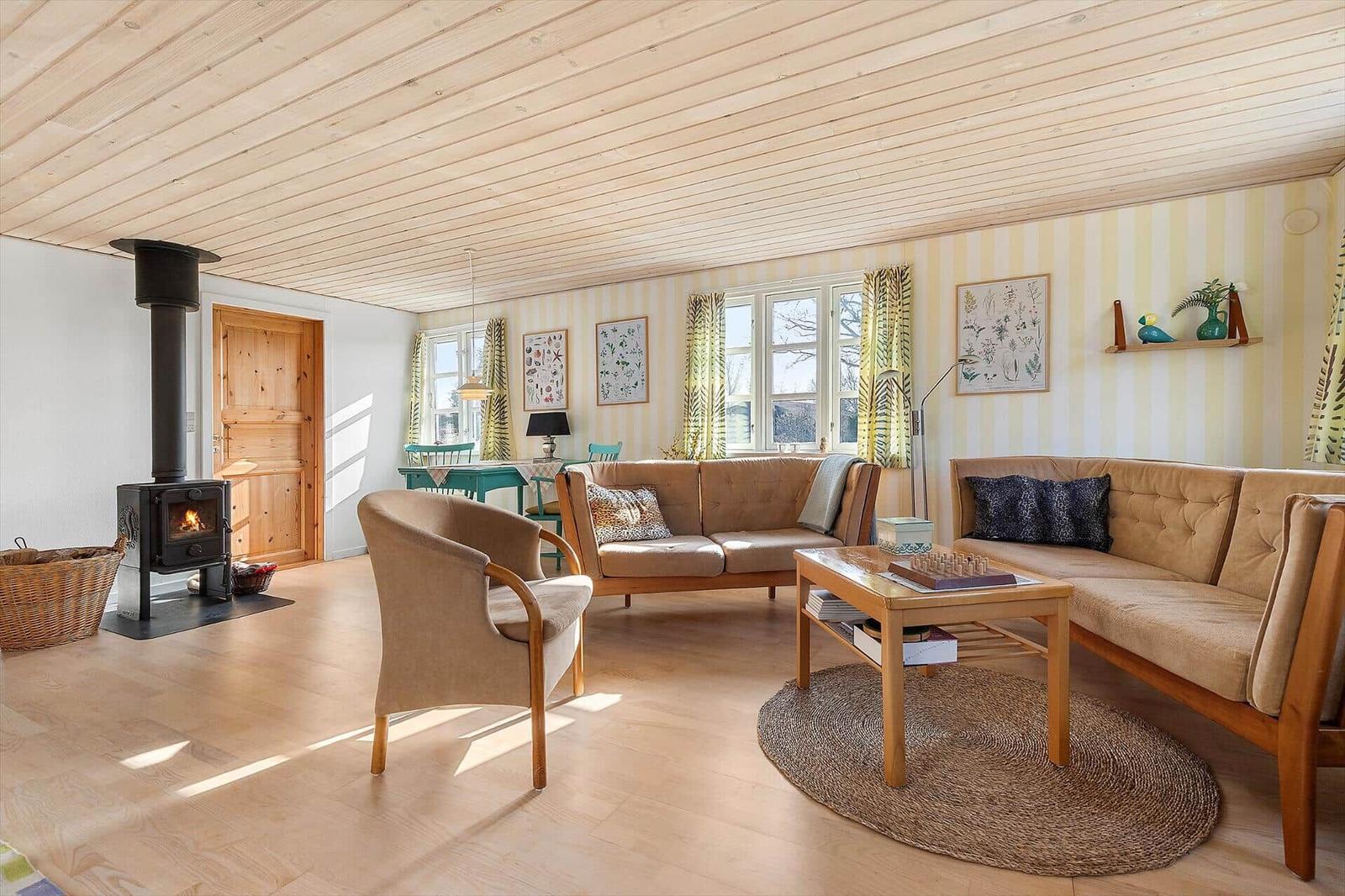 Wohnzimmer mit Holzdecke, Kamin und Sofa. Fenster mit Vorhängen und Wandbilder.