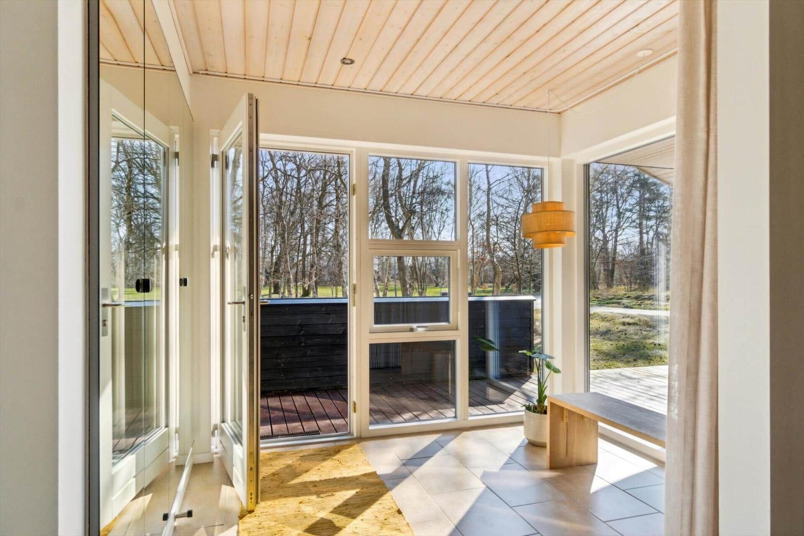 Helle Terrasse mit Glaswänden und Holzdecke. Blick auf Wald und Holzterrasse.