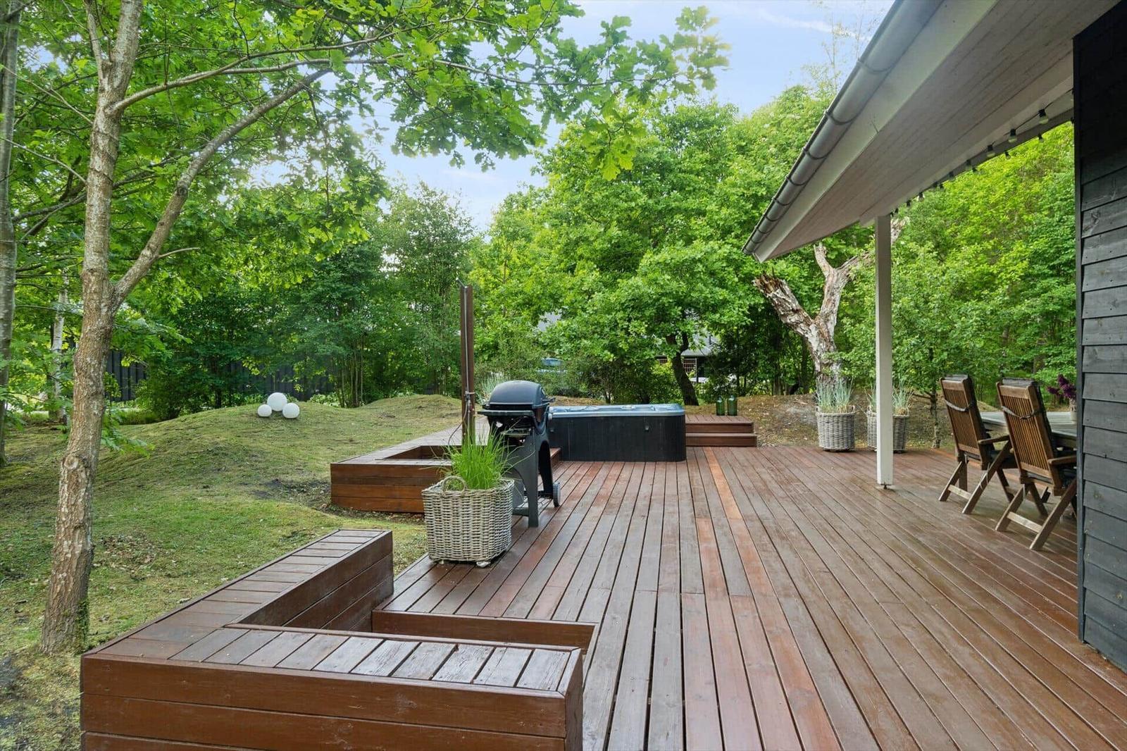 Holzterrasse mit Grill, Whirlpool und Sitzgelegenheiten im Grünen.