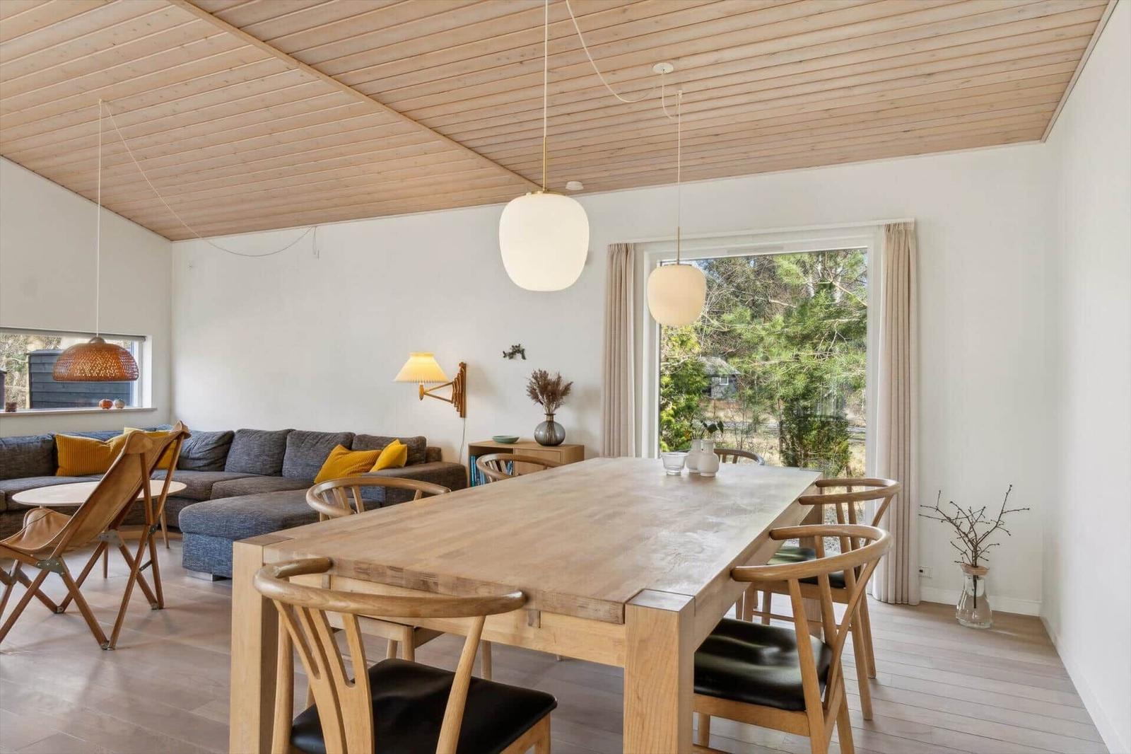Essbereich mit Holztisch und Stühlen, Wohnbereich mit Sofa und Fensterblick.