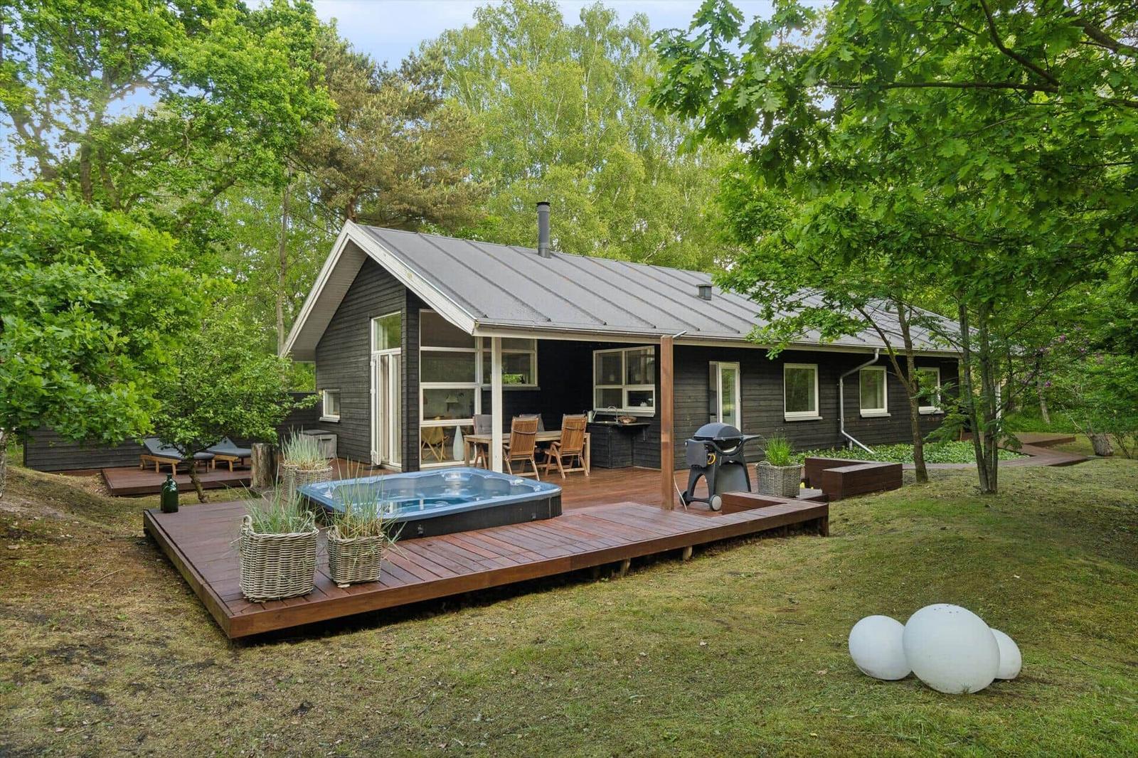 Holzterrasse mit Whirlpool, Grill und Sitzgelegenheiten um eine moderne Hütte herum.