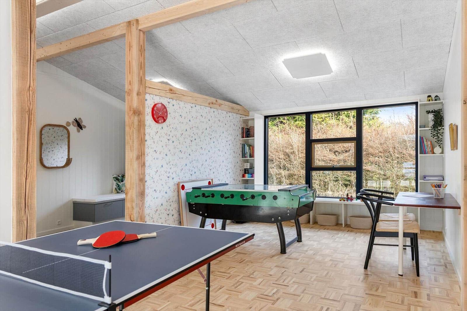 Room with ping pong table, foosball table, and desk. Wooden floor and large windows.
